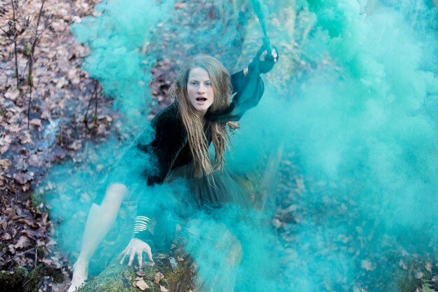 Foto mujer chamán con la mano una bomba de humo verde en el tronco del árbol