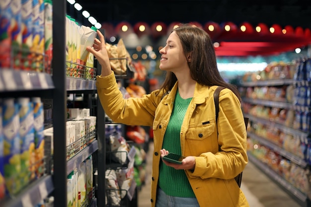 Foto mujer con chaqueta amarilla eligiendo comestibles en el supermercado