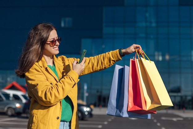 Mujer con chaqueta amarilla está tomando fotos con un teléfono inteligente de bolsas de compras