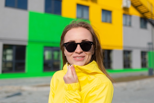 Mujer en una chaqueta amarilla y con gafas de sol sonriendo con fondo de edificios de colores brillantes