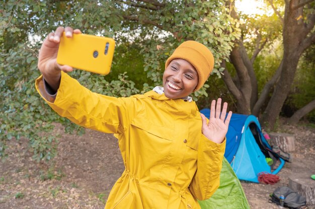 Foto una mujer con una chaqueta amarilla está tomando una selfie con su teléfono celular rodeada de naturaleza