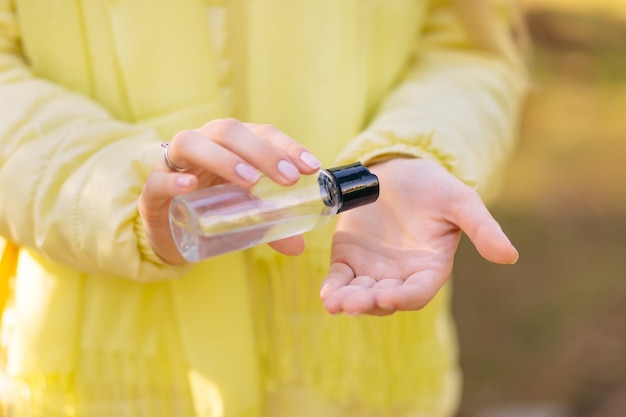 Mujer en una chaqueta amarilla trata las manos con un spray antiséptico