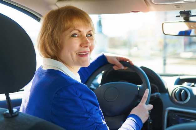 Una mujer con una chaqueta azul conduciendo un automóvil atravesando la ciudad.