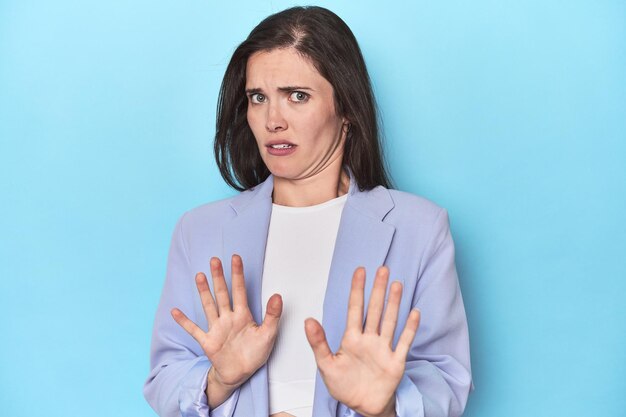 Mujer con chaqueta azul sobre fondo azul rechazando a alguien mostrando un gesto de disgusto