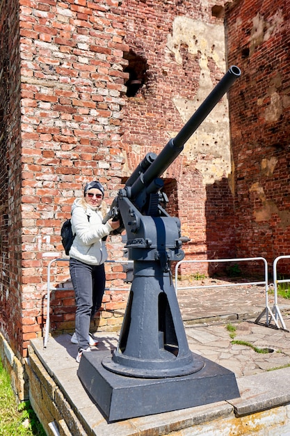 Una mujer con una chaqueta blanca cerca de un cañón antiaéreo de la segunda guerra mundial