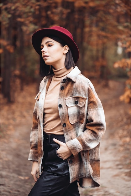 Una mujer con una chaqueta a cuadros y un sombrero se para en el bosque de otoño