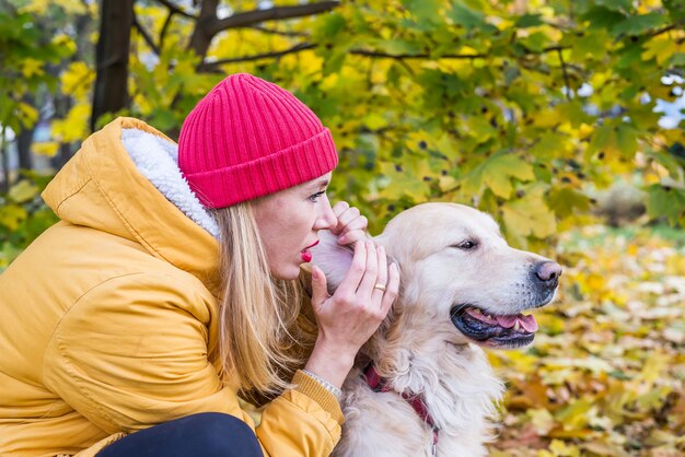 La mujer de la chaqueta le dice algo en un susurro al oído al perro perdiguero. Mujer y perro en otoño de hojas amarillas.