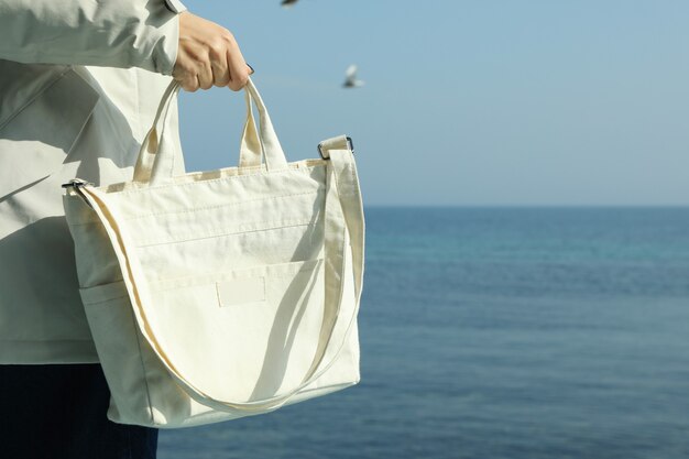 Mujer en chaqueta con elegante bolso ecológico contra el mar