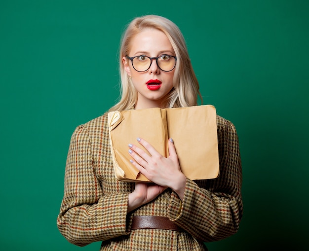 Mujer en chaqueta de estilo británico con libro sobre pared verde