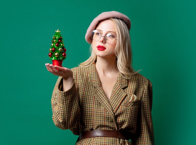 Mujer con chaqueta de estilo y sombrero con árbol de Navidad en pared verde