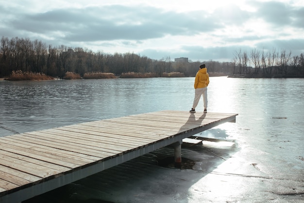 Mujer en una chaqueta de invierno amarilla contra un río