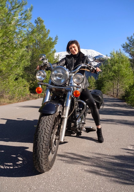 Una mujer con una chaqueta de motociclista de cuero negro en una motocicleta chopper en Grecia en una carretera en el bosque