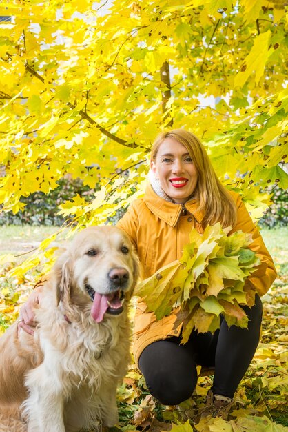 Mujer en una chaqueta y un perro perdiguero entre hojas amarillas de otoño en el parque.