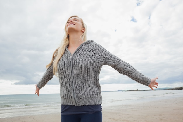 Mujer en chaqueta de punto gris estirando los brazos en la playa