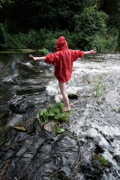 mujer en chaqueta roja impermeable vadeando el río de montaña