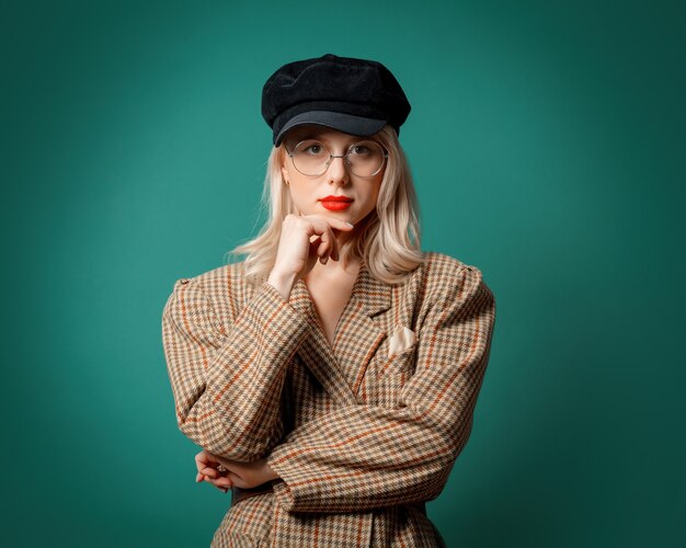 Mujer con chaqueta y sombrero de estilo británico en la pared verde