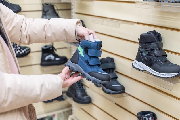 Una mujer con chaqueta en una tienda examina los cálidos zapatos de los niños.