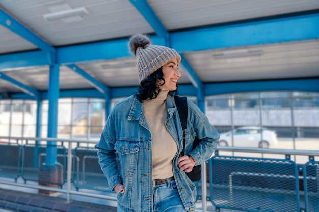 mujer con chaqueta vaquera está hablando por teléfono y esperando un autobús de tranvía en la parada Foto de estilo de vida