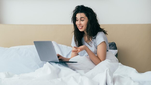 Mujer de chat de video en línea por la mañana usando una cama portátil