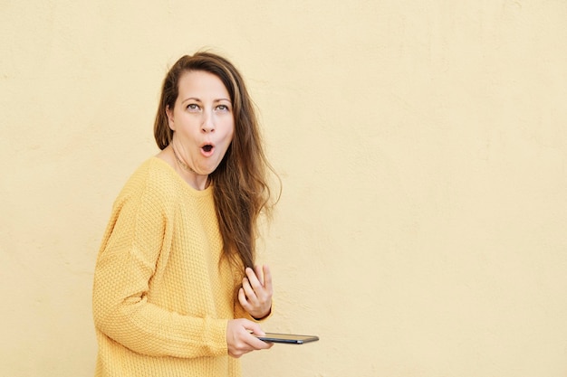 Mujer chateando en su teléfono inteligente con una expresión de asombro mientras mira a la cámara