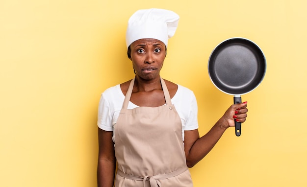 Mujer chef afro negra que parece desconcertada y confundida, mordiendo el labio con un gesto nervioso, sin saber la respuesta al problema