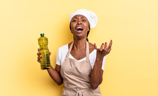 Mujer chef afro negra que parece desesperada y frustrada, estresada, infeliz y molesta, gritando y gritando. concepto de aceite de oliva