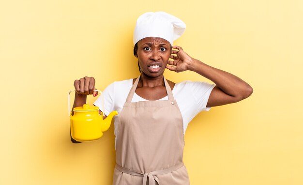 Mujer chef afro negra que se siente estresada, preocupada, ansiosa o asustada, con las manos en la cabeza, en pánico por el error. concepto de tetera