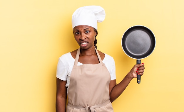 Mujer chef afro negra que se siente perpleja y confundida, con una expresión tonta y atónita mirando algo inesperado