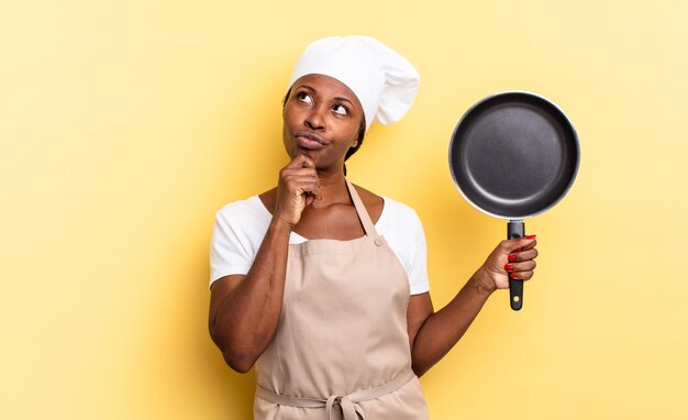 Mujer de chef afro negro pensando, sintiéndose dudoso y confundido, con diferentes opciones, preguntándose qué decisión tomar