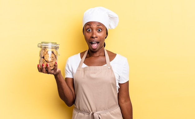 Mujer de chef afro negro que parece muy conmocionada o sorprendida, mirando con la boca abierta diciendo wow. concepto de cookies
