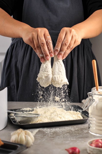 Mujer chef casera haciendo pollo frito crujiente casero, cubriendo palitos de pollo con harina en la cocina