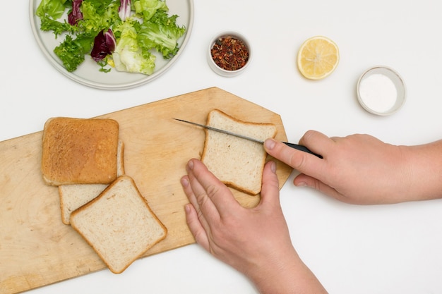 La mujer chef está cocinando, cortando pan para freír picatostes y agregando a las hojas de ensalada.