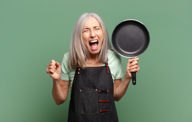 Mujer de chef de mediana edad bastante pelo gris con una sartén