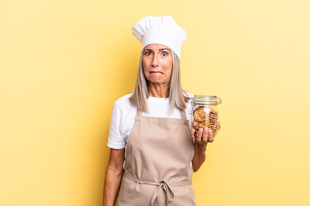 Mujer chef de mediana edad que mira perpleja y confundida, mordiendo el labio con un gesto nervioso, sin saber la respuesta al problema con las galletas