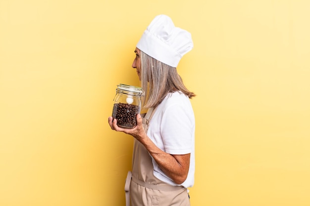 Mujer chef de mediana edad en la vista de perfil que busca copiar el espacio por delante, pensando, imaginando o soñando despierta sosteniendo granos de café