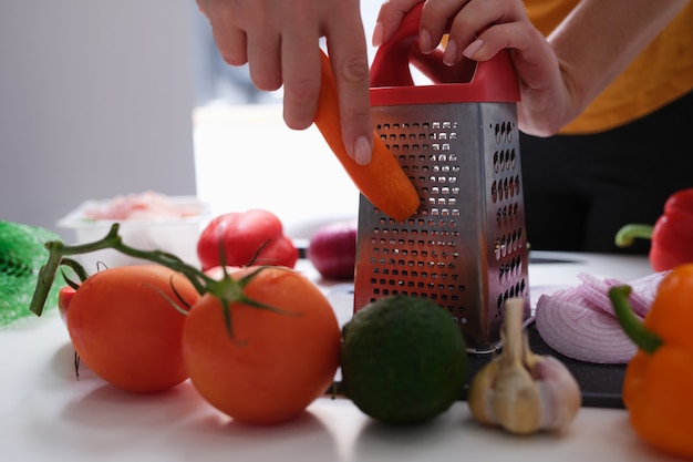 Mujer chef rallar zanahorias en la mesa con verduras closeup