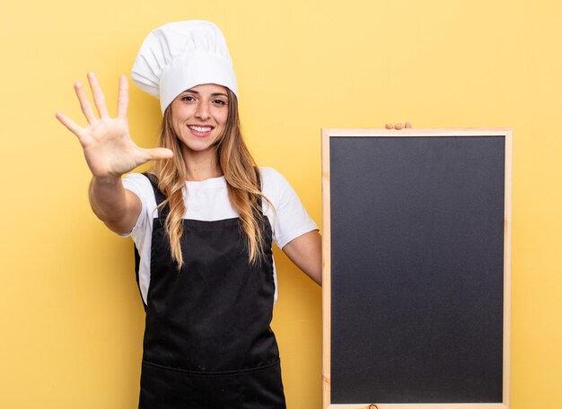 Mujer chef sonriendo y luciendo amigable, mostrando el número cinco. concepto de menú de pizarra