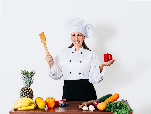 Mujer chef sosteniendo un cucharón sobre una mesa con verduras Una mujer sonriente chef sosteniendo un cucharón y verduras retrato de una mujer chef sosteniendo un cucharón sobre un fondo aislado