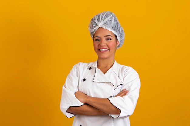 Mujer chef con uniforme y capó de pie con los brazos cruzados y posando sobre un aislado concepto de ocupación de fondo amarillo