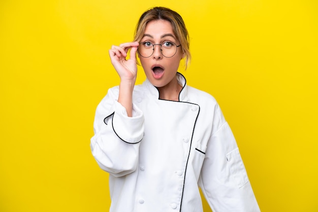 Mujer chef uruguaya aislada de fondo amarillo con gafas y sorprendida