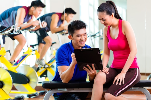 Mujer china asiática y entrenador personal de fitness en el gimnasio discutiendo el horario de entrenamiento y los objetivos de entrenamiento