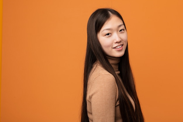 La mujer china bastante joven mira a un lado sonriente, alegre y agradable.