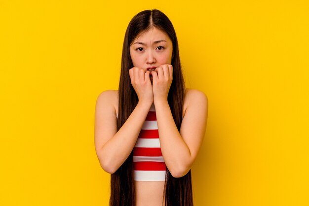 Mujer china joven aislada en la pared amarilla mordiéndose las uñas, nerviosa y muy ansiosa.