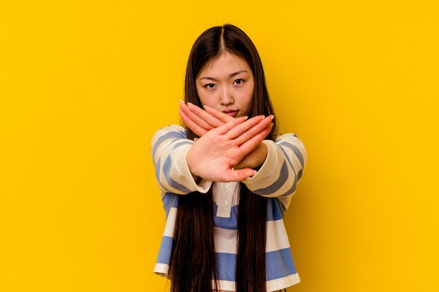 Mujer china joven aislada en la pared amarilla que se coloca con la mano extendida que muestra la señal de pare, previniéndole.