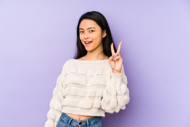 Mujer china joven aislada en una pared púrpura que muestra el signo de la victoria y una amplia sonrisa.