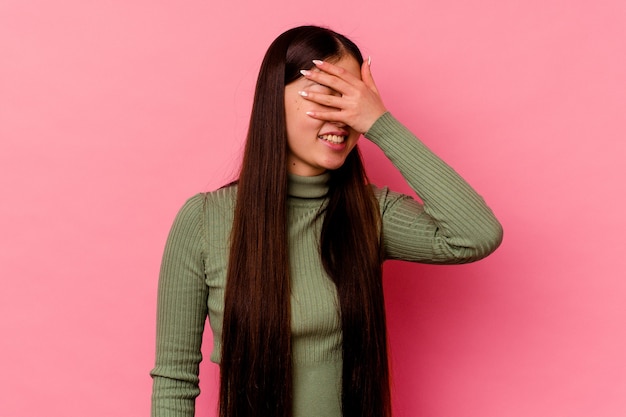 La mujer china joven aislada en la pared rosada cubre los ojos con las manos, sonríe ampliamente esperando una sorpresa.