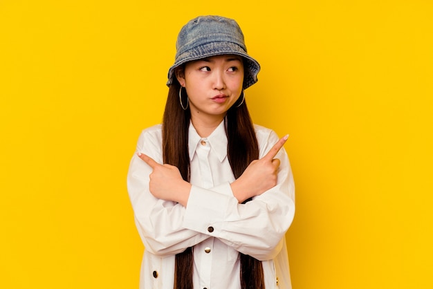 La mujer china joven aislada en los puntos amarillos hacia los lados, está tratando de elegir entre dos opciones.