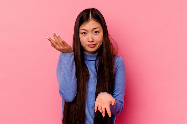 La mujer china joven aislada en rosa hace escala con los brazos, se siente feliz y confiada.