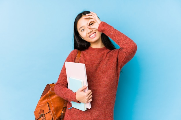 La mujer china joven del estudiante aislada excitó guardar gesto aceptable en ojo.