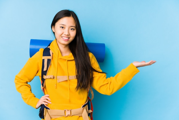 Mujer china joven del mochilero que muestra un espacio en blanco en una palma y que lleva a cabo otra mano en la cintura.